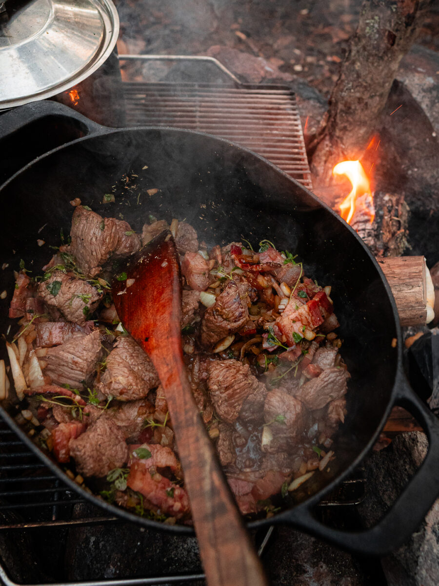 Höstgryta med kött och lök som puttrar över öppen eld