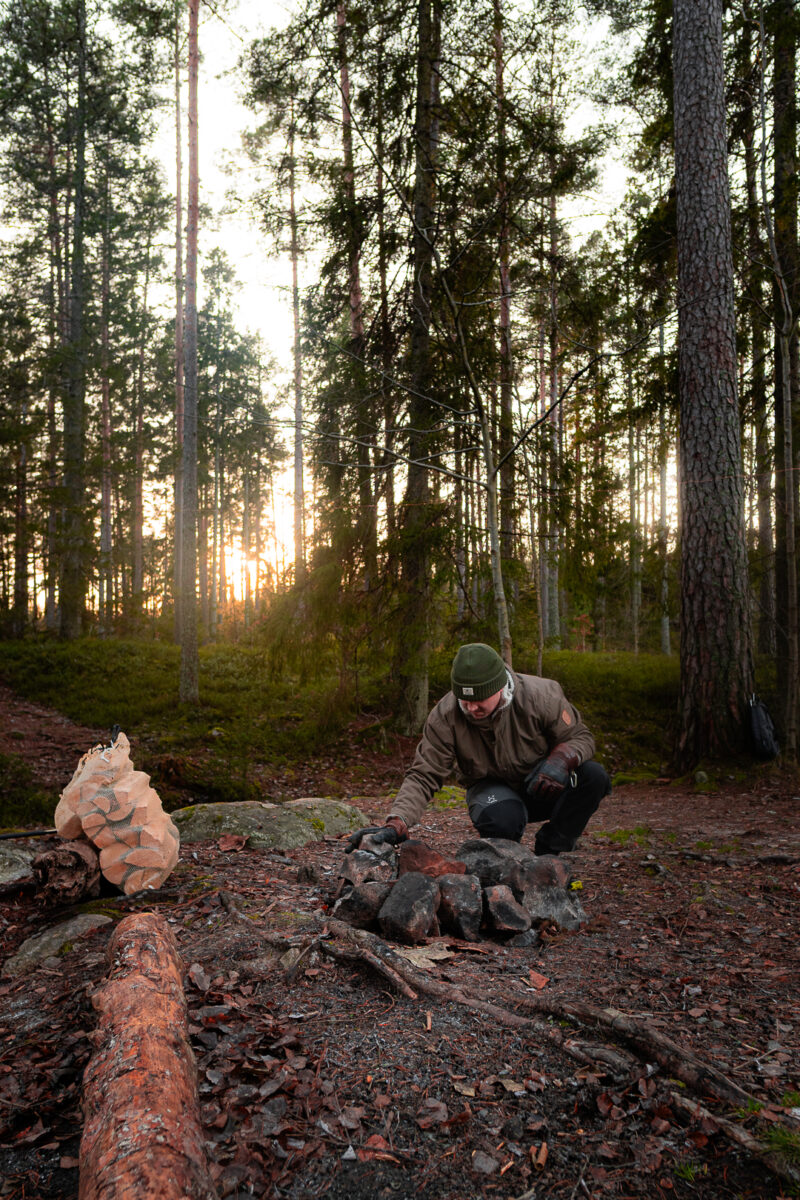 Man tänder en eld i tallskogen i lågt eftermiddagsljus