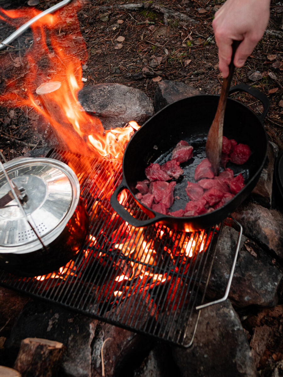 Kött bryns i en gjutjärnsgryta på ett galler över öppen eld
