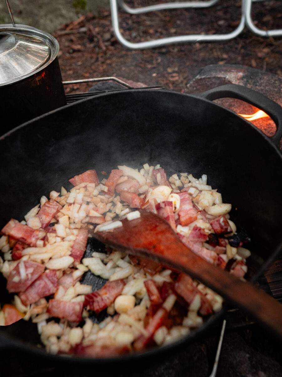 Pancetta och lök fräses i en gjutjärnsgryta över elden
