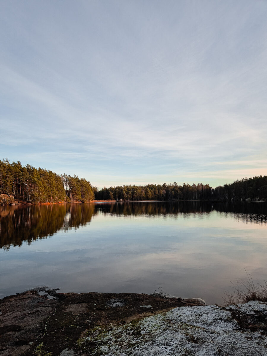 Stilla skogssjö med frost på klipphällen i novemberljus
