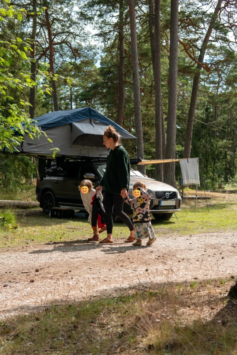 2 barn och en förälder går framför en bil med taktält utfällt