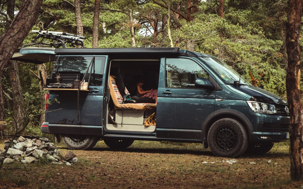 VW T6 California med skjutdörren öppen parkerad i tallskogen. Gotland med campervan