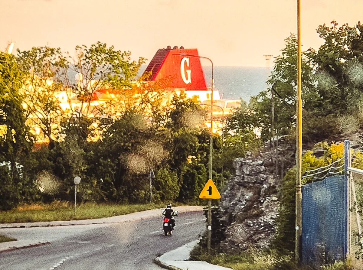 Gotlandsfärjans röda skorsten bakom träden i kvällsljus