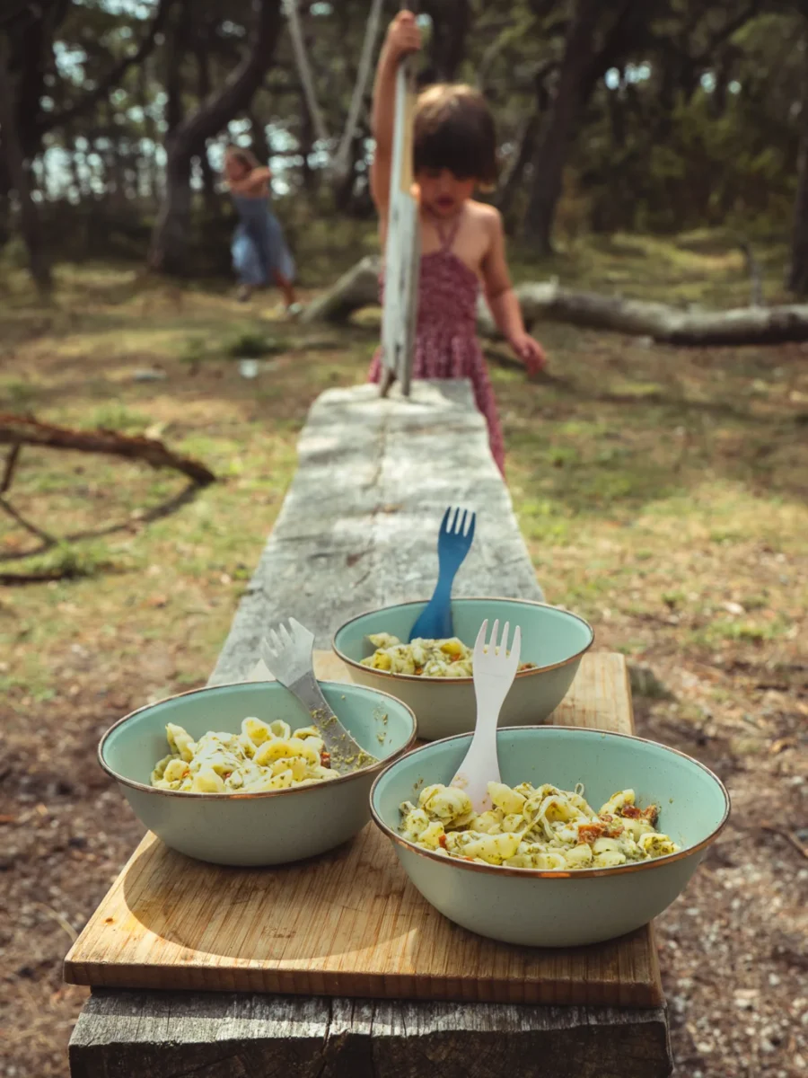 Skålar med pasta pesto på ett bord i skogen medan ett barn leker i bakgrunden